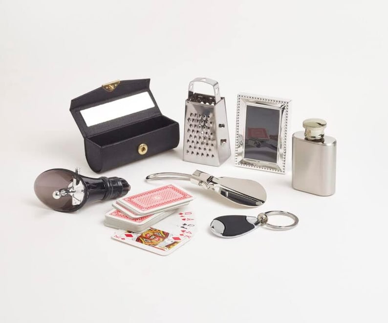 May include: An assortment of small items including a black leather glasses case, a stainless steel grater, a silver picture frame, a silver flask, a bottle stopper, a deck of playing cards, a shoe horn, and a keychain.