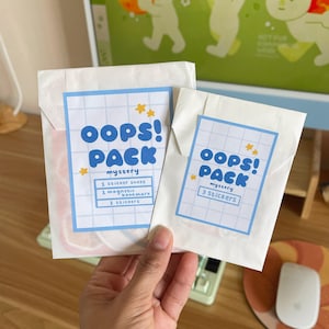 May include: Two white paper packs with blue and white labels that read "OOPS! PACK mystery" with the contents listed below. One pack contains a sticker sheet, magnetic bookmark, and two stickers. The other pack contains three stickers.