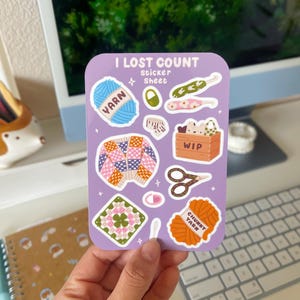 May include: A sticker sheet with a purple background and various illustrations related to knitting and crocheting. The sheet includes yarn balls, knitting needles, a crochet square, scissors, and a basket labeled "WIP". The text "I Lost Count Sticker Sheet" is at the top of the sheet.