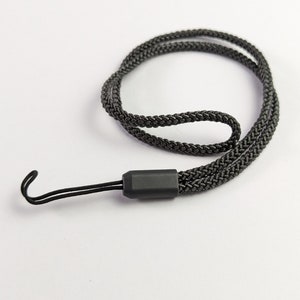 May include: A black braided nylon lanyard featuring a sturdy cord loop at one end and a matte black plastic connector piece. The cord is woven in a tight, durable pattern, forming a continuous loop that is designed for securing small items.