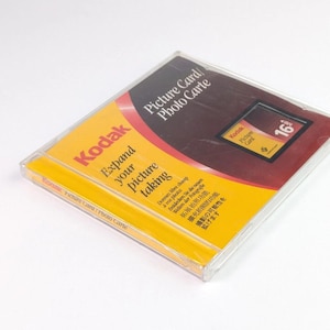 May include: A Kodak Picture Card in a transparent plastic case. The card features a yellow and red design with the Kodak logo and the text "Expand your picture taking." The card also has the text "Picture Card / Photo Carte."