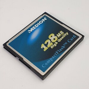 May include: A black and blue Medion CompactFlash card with the text "128 MB High Quality" and "CompactFlash Card". The card has a black frame and a blue and white gradient background.