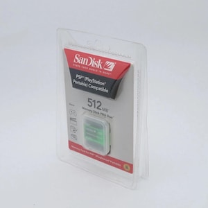 Pode incluir: Um Memory Stick PRO Duo Sandisk de 512MB para PSP (PlayStation Portable) em embalagem plástica transparente. A embalagem tem um detalhe em vermelho e preto com o logotipo Sandisk e informações do produto.
