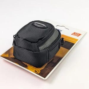 Pode incluir: Uma bolsa para câmara Vanguard preta e cinzenta com exterior em tecido texturizado, fecho de correr e um emblema oval da marca no topo. A bolsa está fixada num cartão de apresentação branco com um ícone laranja de resistência.