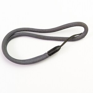 Pode incluir: Um cordão trançado cinza-escuro com uma peça de conexão de plástico preto lisa e arredondada que prende as duas extremidades da corda. O cordão é formado em um laço alongado, exibindo uma construção de tecido trançado texturizado.