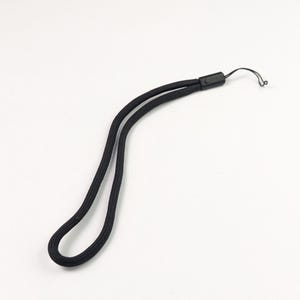 Pode incluir: Uma alça de pulso preta com um design de cordão trançado. A tira é fixada por uma pequena peça de conexão de plástico preto, que transita para um cordão de laço preto fino e flexível, projetado para fixação em vários pequenos dispositivos eletrônicos.