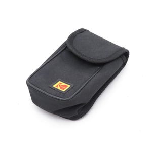 Może przedstawiać: Czarny futerał na aparat z klapką. Etui ma prostokątny kształt z zaokrągloną górą i małym, żółto-czerwonym logo Kodak z przodu. Etui wykonane jest z teksturowanej tkaniny.