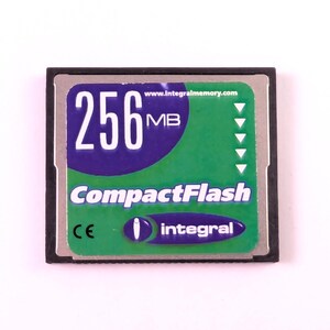 May include: A CompactFlash memory card with a black border. The card has a green and blue label with the text "256 MB" and "CompactFlash". The brand name "integral" is also visible.