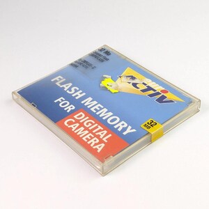 May include: A clear plastic case containing a flash memory card for a digital camera. The card has a blue and orange label with the text "FLASH MEMORY FOR DIGITAL CAMERA" and a yellow sticker indicating 32 MB.