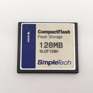 Könnte beinhalten: Eine schwarz-weiße SimpleTech CompactFlash-Speicherkarte mit 128 MB Speicherkapazität. Das Etikett enthält den Text CompactFlash Flash Storage, 128MB, SLCF128H und SimpleTech sowie einen blauen vertikalen Streifen auf der linken Seite mit der Aufschrift INSERT.
