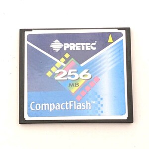 May include: A square Pretec CompactFlash memory card with a black frame and a blue label. The label features the text PRETEC, 256 MB, and CompactFlash, along with a graphic design of a colorful diamond shape and diagonal lines in white and yellow.