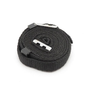 May include: A coiled black nylon strap with two metal clasps. The strap is tightly wound, showing its woven texture. The clasps are silver-coloured and rectangular, designed for secure fastening. The background is plain white.