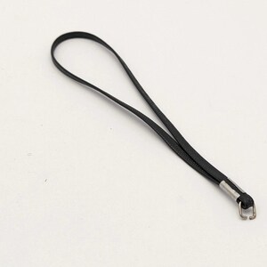 Pode incluir: Uma alça de cordão preta com uma tira fina e flexível formada num laço contínuo. As extremidades do cordão são fixadas por um grampo de metal prateado, que se liga a um pequeno gancho de metal retangular de cor prateada.