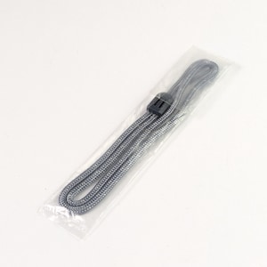 Pode incluir: Um cordão trançado cinza com um fecho deslizante ajustável de plástico preto, envolto em uma capa protetora de plástico transparente. O cordão está dobrado em um laço longo e estreito, exibindo um padrão tecido texturizado em toda a extensão.