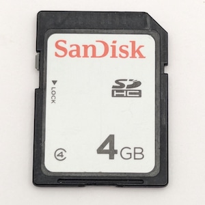 Peut inclure: Une carte mémoire SDHC SanDisk noire avec une étiquette blanche. L'étiquette présente le logo SanDisk rouge, le symbole SDHC, un chiffre 4 dans un cercle et le texte 4GB. Un petit interrupteur de verrouillage gris est visible sur le côté gauche.