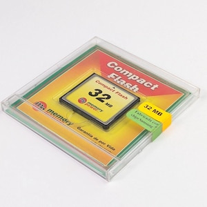 May include: A Compact Flash memory card, 32 MB, in a clear plastic case. The card is black with yellow and black text. The packaging includes the text "Compact Flash" and "memory power". A yellow and green sticker reads "32 MB".