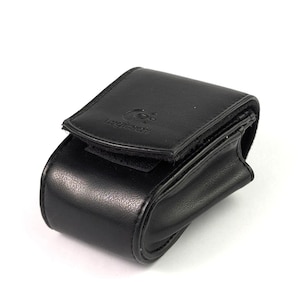 Puede incluir: Una funda de cuero negro con cierre de solapa. La funda tiene forma rectangular con bordes redondeados y un pequeño logotipo en la solapa. La funda parece ser para un pequeño dispositivo electrónico.