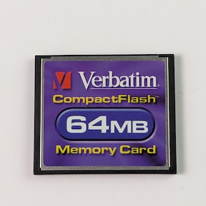 May include: A Verbatim CompactFlash 64MB memory card. The card features a purple and black design, with the Verbatim logo in red and white. The text "CompactFlash" and "Memory Card" are in yellow.