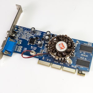 Puede incluir: Una tarjeta gráfica de ordenador azul con un ventilador y un conector VGA. El ventilador tiene un logotipo rojo y blanco. La tarjeta tiene varios chips y conectores. La tarjeta mide aproximadamente 15 cm de largo.
