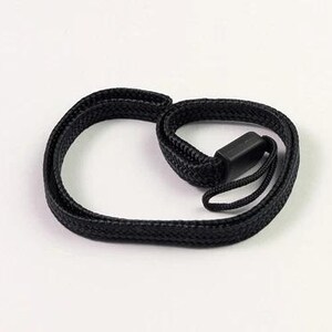 May include: A black woven wrist strap with a plastic clasp. The strap is looped and appears to be made of a durable, braided material. The clasp is rectangular and secures the strap. The wrist strap is designed to be worn around the wrist.