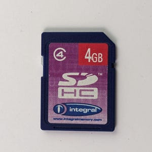 Può includere: Una scheda di memoria SDHC blu con un'etichetta viola e rossa. L'etichetta mostra "4GB" e il logo "SDHC". Il marchio "integral" e l'indirizzo del sito web sono anch'essi visibili.
