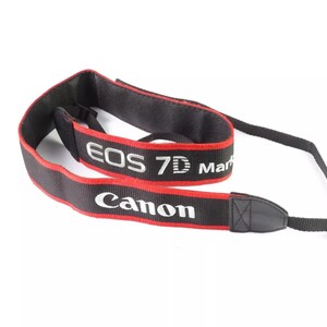 Può includere: Tracolla per fotocamera nera e rossa con testo bianco che recita "Canon EOS 7D Mark".