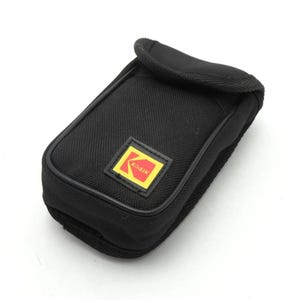 Pode incluir: Estojo de câmera preto com o logotipo Kodak. O estojo é retangular com uma parte superior curva e uma pequena aba. O logotipo Kodak é um quadrado amarelo com borda vermelha e o nome Kodak.