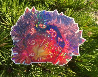 Pode incluir: Um autocolante holográfico com um dado D20 com um design de galáxia, rodeado por elementos florais vermelhos e roxos. Os números do dado são delineados em laranja. O autocolante tem um acabamento brilhante e iridescente.
