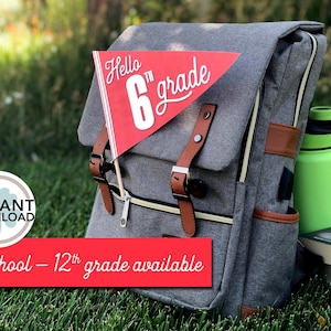 May include: A gray backpack with brown leather accents and a red pennant flag that says "Hello 6th grade". The backpack is sitting on green grass with a green water bottle and a stack of books.
