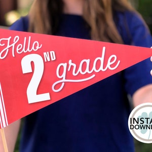 May include: Red and white pennant with the text "Hello 2nd grade" in white. The pennant is held by a person's hand.