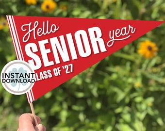 Peut inclure: Un fanion rouge avec l'inscription blanche "Hello SENIOR year" et "CLASS OF '27". Un cercle avec "INSTANT DOWNLOAD" est également présent. Le fanion est tenu par un bâton en bois.