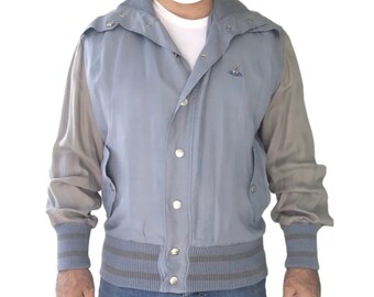 May include: A light blue and gray baseball jacket with a button closure and a small logo on the chest. The jacket has a hood and ribbed cuffs and waistband.