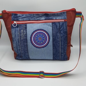 Könnte beinhalten: Eine Jeans-Umhängetasche mit roter Netz-Seitenwand und einem Regenbogenriemen. Die Tasche hat eine zentrale Jeans-Panel mit einem gestickten kreisförmigen Design in Blau, Rot und Gelb. Die Tasche hat einen Reißverschluss und der Text "DENIM" ist sichtbar.