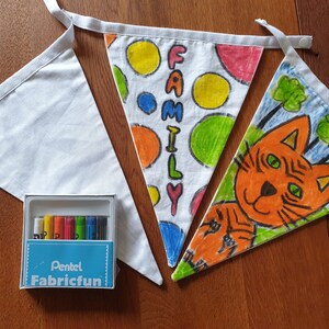May include: Three white fabric bunting flags, two decorated with colourful drawings and the word "FAMILY". A box of Pentel Fabricfun markers is included. One flag features a cat illustration.