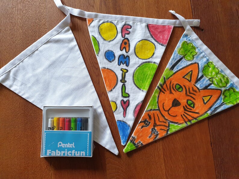 May include: Three white fabric bunting flags, two decorated with colourful drawings and the word "FAMILY". A box of Pentel Fabricfun markers is included. One flag features a cat illustration.