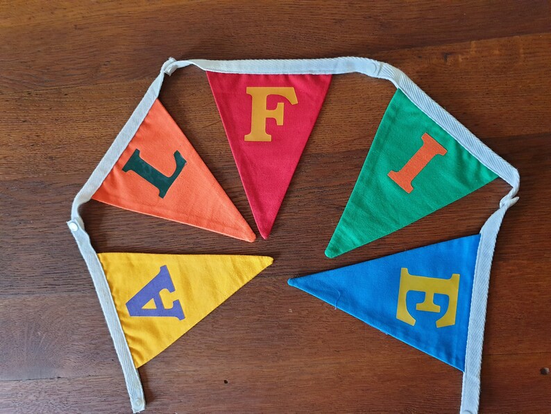May include: A colourful felt banner with the word "FIFE" spelled out in different coloured letters. Each letter is on a separate triangular flag. The flags are connected by a white string.