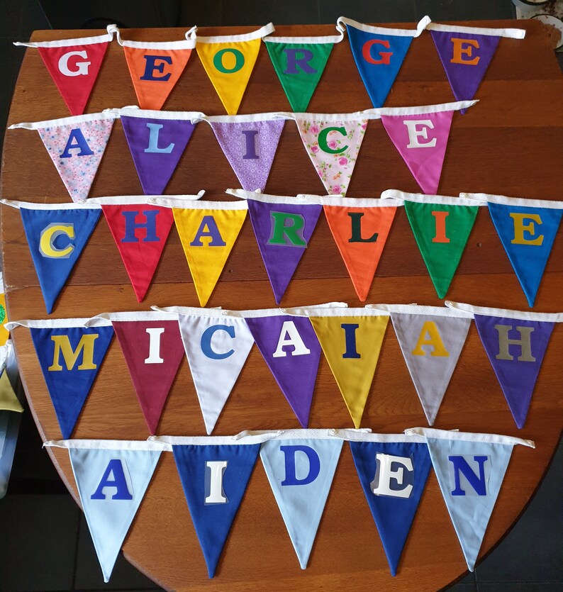 May include: A colourful bunting with the names George, Alice, Charlie, Micah, and Aiden spelled out in felt letters. Each letter is on a separate triangular flag.