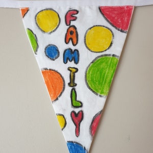 May include: A triangular fabric banner with a white background, featuring a polka dot design in various colours and the word "FAMILY" written vertically. The banner has a white ribbon for hanging. The polka dots include yellow, green, red, and blue.