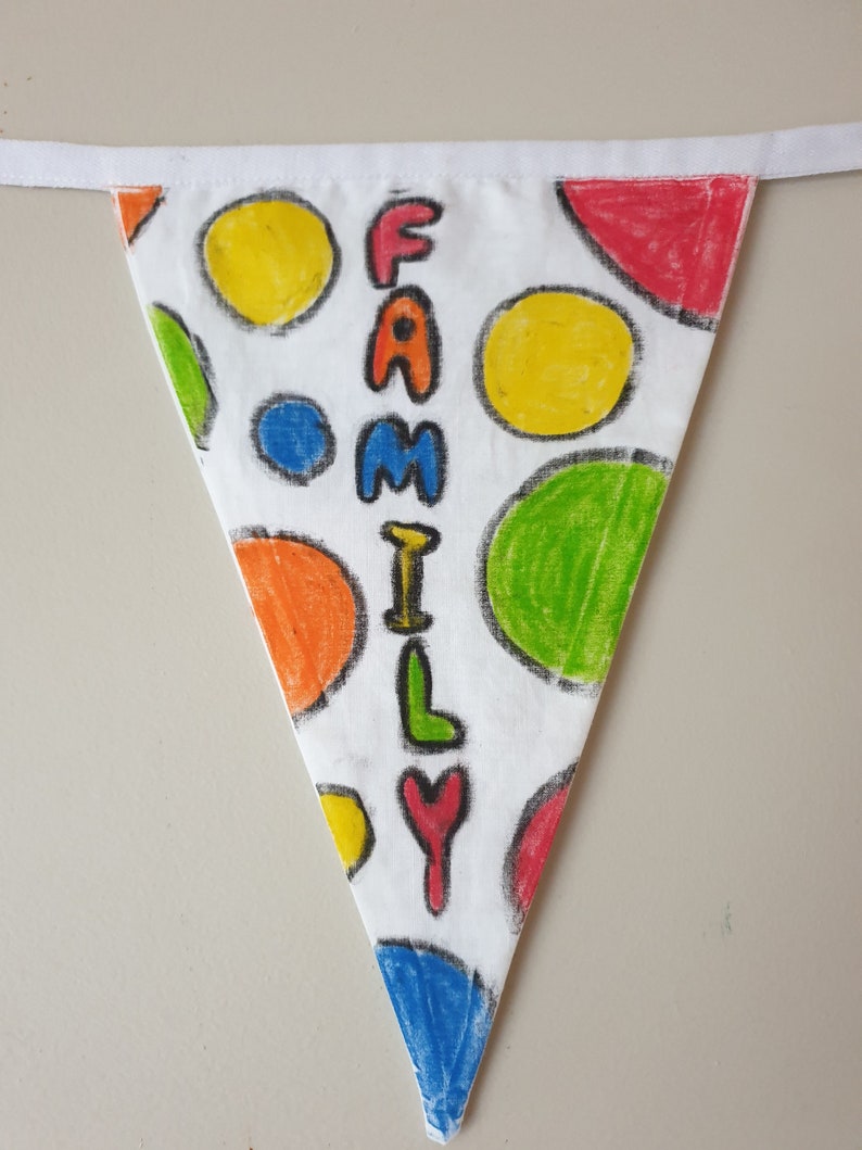 May include: A triangular fabric banner with a white background, featuring a polka dot design in various colours and the word "FAMILY" written vertically. The banner has a white ribbon for hanging. The polka dots include yellow, green, red, and blue.