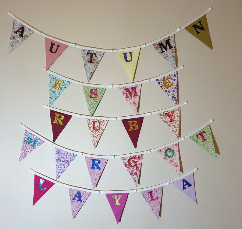 May include: A colourful fabric banner with the letters "AUTUMN" spelled out in black letters on a white background. The banner is made of different patterned fabrics and is strung together with white string.