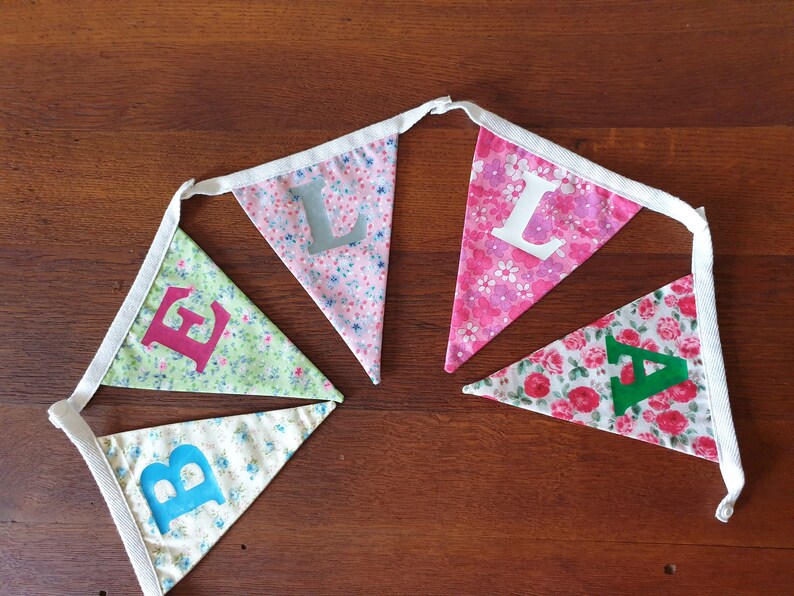 May include: A bunting with five flags, each with a different floral pattern and a letter on it. The letters spell out "BELLA".
