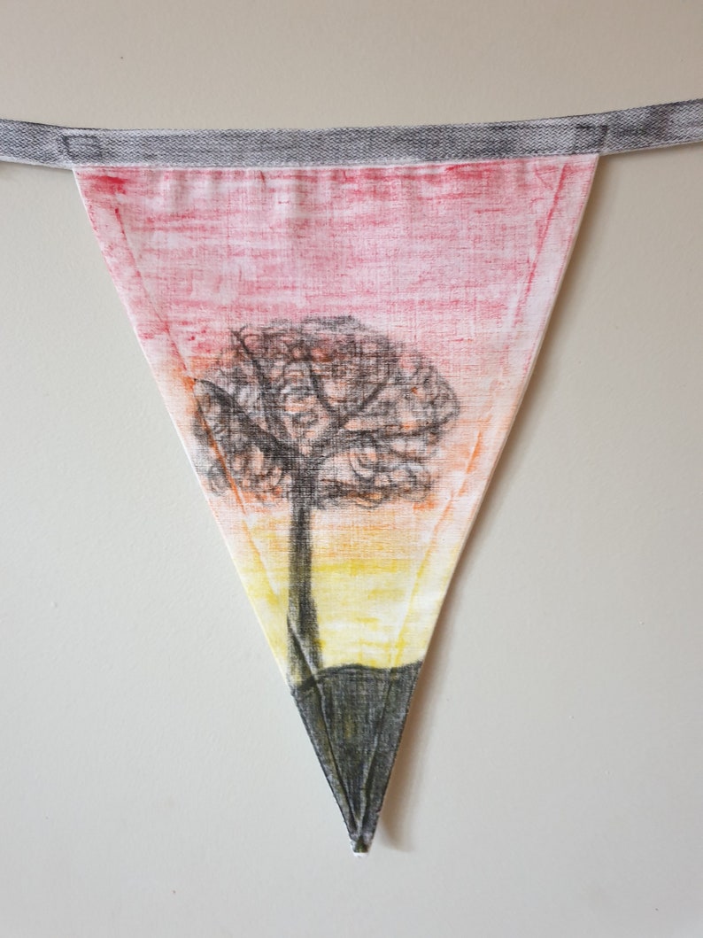 May include: Triangular fabric bunting with a hand-drawn tree design. The bunting features a sunset-coloured background with a black tree silhouette. It is attached to a grey fabric strip for hanging.