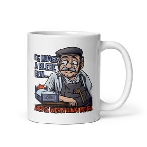 May include: White ceramic mug featuring a cartoon illustration of a man with a mustache and a beret. The mug has text in a blue and white font. The man is leaning on a small bed. The mug has a white handle.