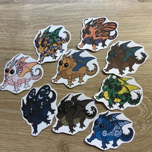 K&ouml;nnte beinhalten: Eine Sammlung von acht gestanzten Aufklebern mit illustrierten Drachen in verschiedenen Farben und Mustern, darunter ein rosa-orangefarbener Drache, ein blau-orangefarbener Drache, ein schwarzer Drache mit Mondsymbolen und ein gr&uuml;n-gelber Drache.