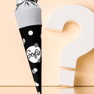 Puede incluir: Una bolsa de regalo c&oacute;nica de lunares blancos y negros con el nombre "Sofie" en un c&iacute;rculo blanco. La parte superior de la bolsa es gris y est&aacute; atada con una cinta plateada. Un gran signo de interrogaci&oacute;n blanco est&aacute; en el fondo.