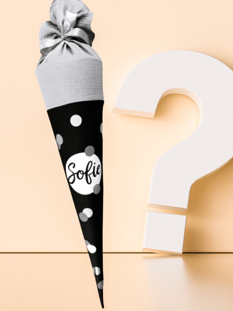 Puede incluir: Una bolsa de regalo c&oacute;nica de lunares blancos y negros con el nombre "Sofie" en un c&iacute;rculo blanco. La parte superior de la bolsa es gris y est&aacute; atada con una cinta plateada. Un gran signo de interrogaci&oacute;n blanco est&aacute; en el fondo.