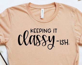 May include: A peach-colored t-shirt with the text "Keeping it classy -ish." printed in black.