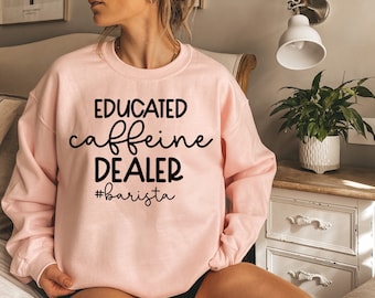 May include: A pink sweatshirt with the text "EDUCATED caffeine DEALER #barista" printed in black.