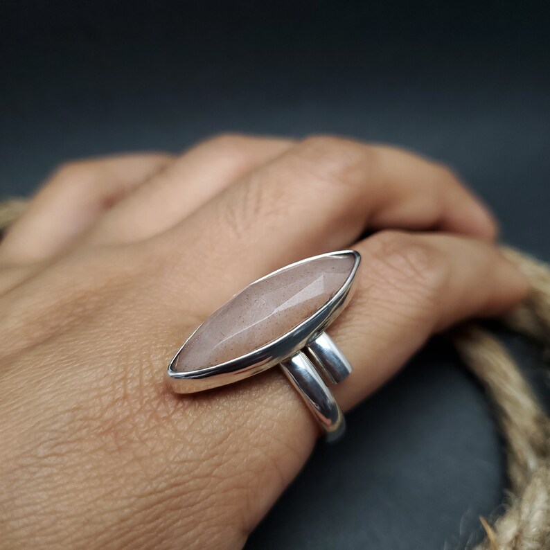 May include: A silver ring featuring a large, elongated, faceted, light pink gemstone. The ring has a modern design with a sleek, polished silver band and a bezel setting that highlights the stone's shape and color.