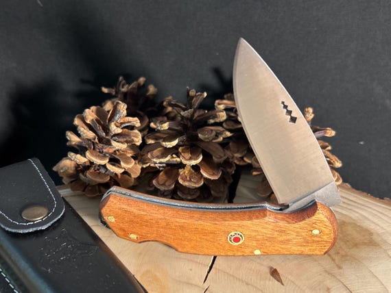 A hand-crafted folding knife with a rich Paduk hardwood handle and leather sheath — the kind of heirloom-quality EDC piece you'd actually pass down.